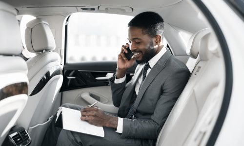 Afro businessman arranging his affairs with notepad in the car, talking on phone